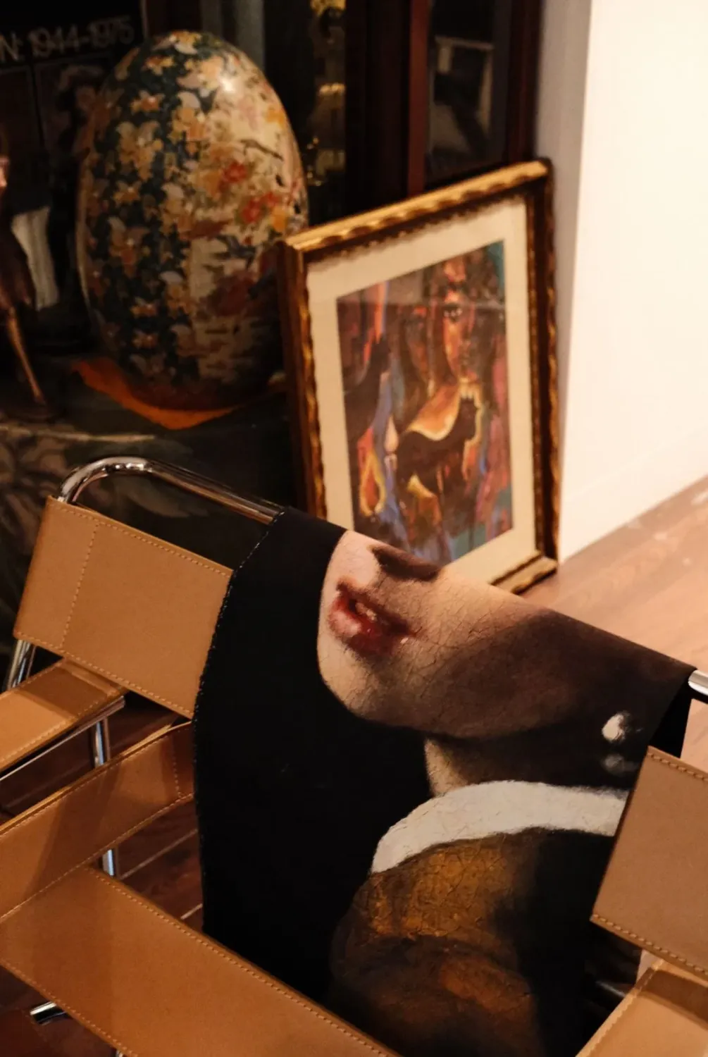 A vintage portrait leaning on a leather chair beside a framed painting